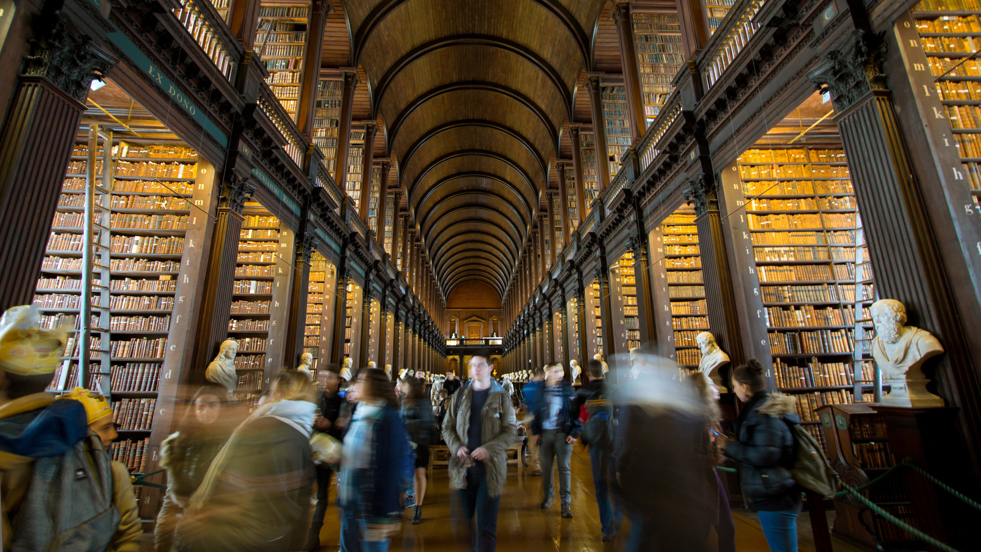 Photo of groups of people walking through Trinity College Dublin's Old Library, looking up at the floor-to-ceiling bookshelves